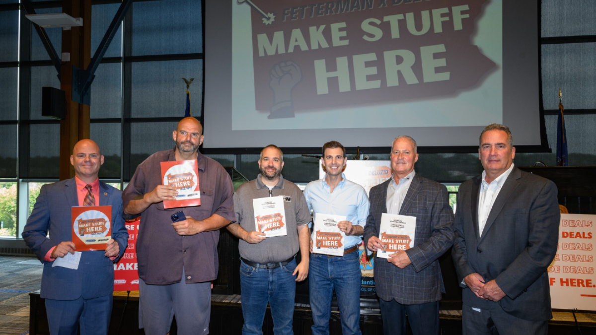 Six men stand together, holding pdfs in front of a large screen that says "MAKE STUFF HERE"