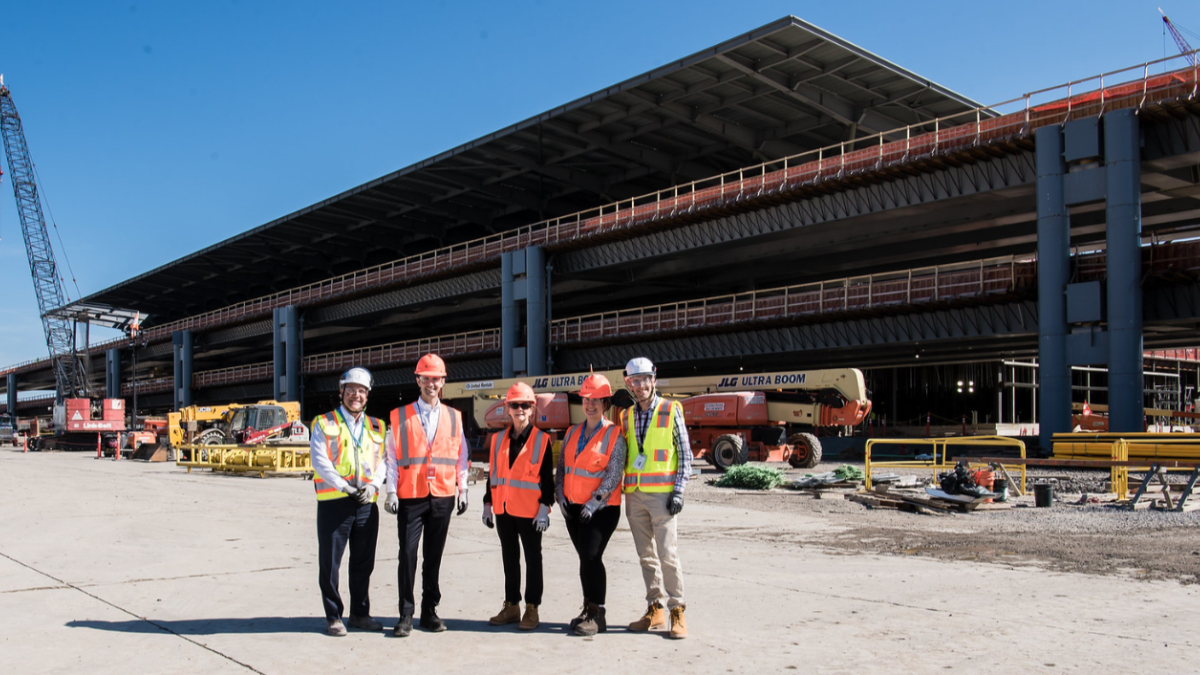 Rep. Deluzio stands with four other people all wearing hard hats as they stand in front of construction at the airport