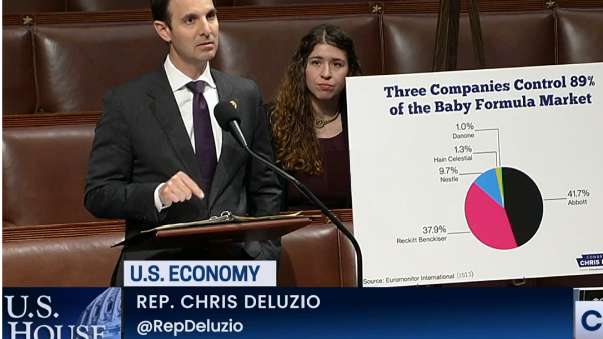 Rep. Deluzio stands behind a podium. A poster is next to him that says, "Work Hard. Play by the Rules. The American Dream."
