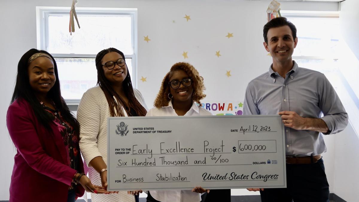 Rep. Deluzio stands with three women behind a large check