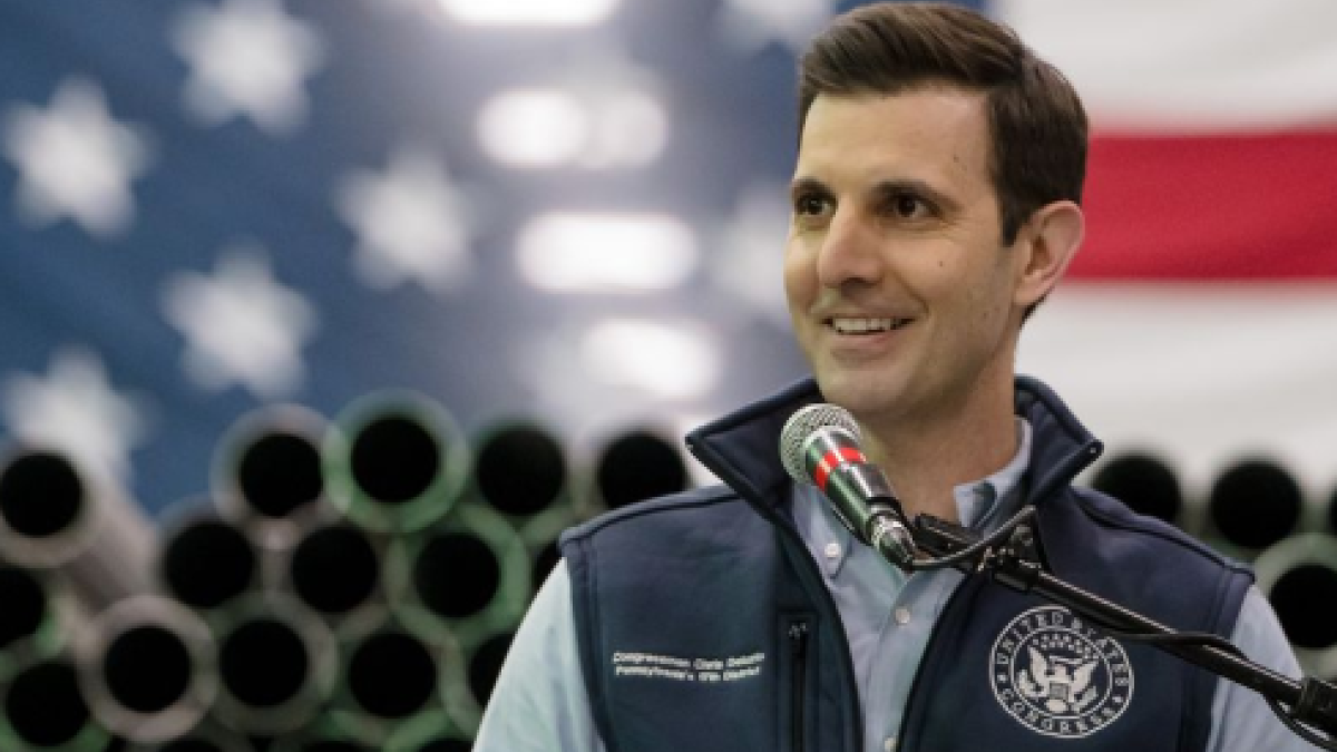 Chris Deluzio smiles, standing at a podium with a flag behind him
