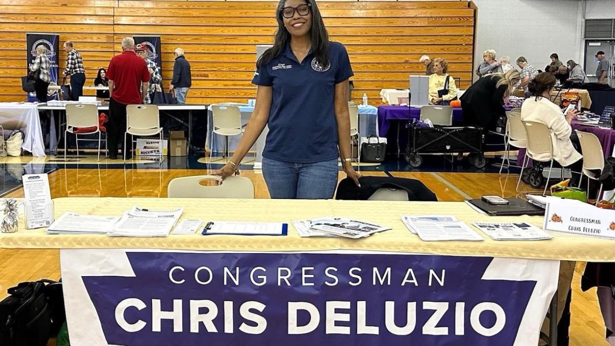 A team Deluzio member stands behind a table in a gymnasium 