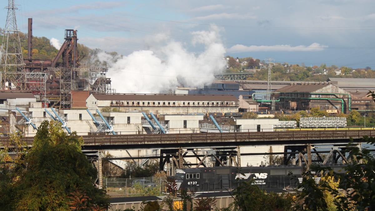 A steel factory in Western PA pumps out smoke. A train runs in front of it.