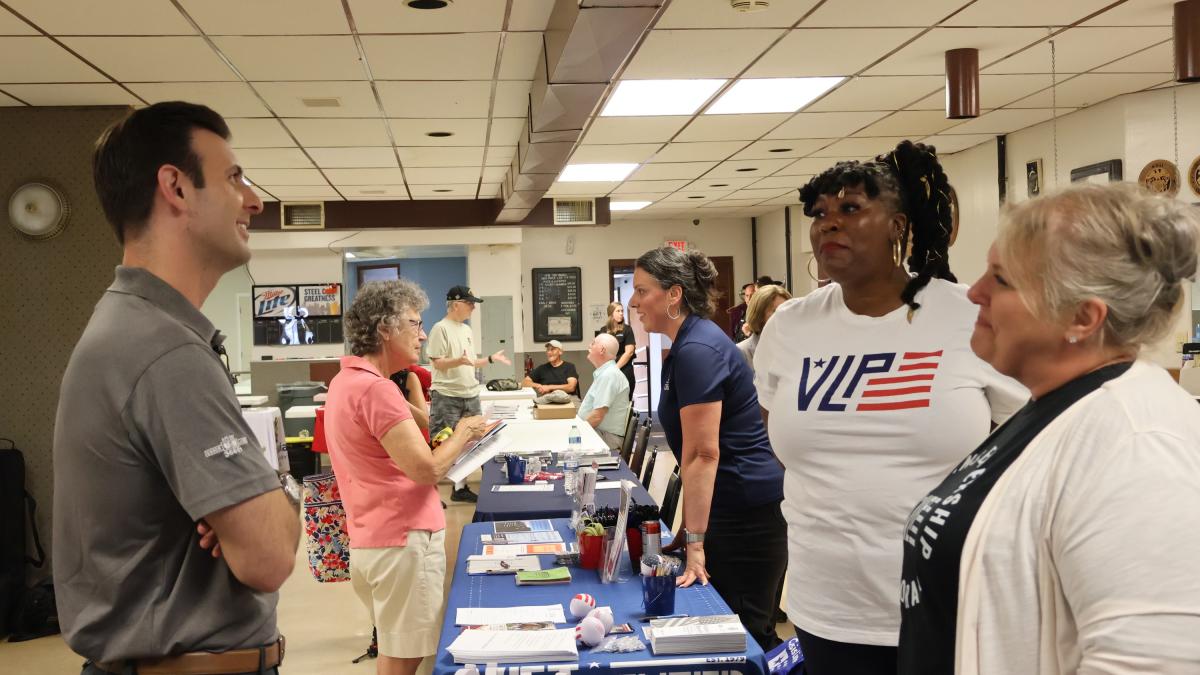 Rep. Deluzio speaks to two women behind a table with resources for veterans
