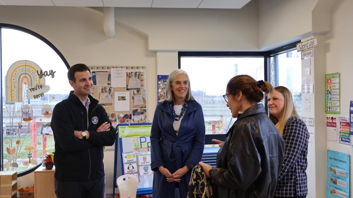 Rep. Deluzio stands next to three women in a pre school classroom. They are between two large windows. 