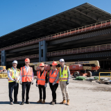 Rep. Deluzio stands with four other people all wearing hard hats as they stand in front of construction at the airport
