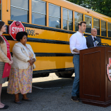 Rep. Deluzio stands behind a podium, in front of an electric school bus and gives remarks. Three other people stand behind him. 