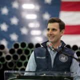 Chris Deluzio smiles, standing at a podium with a flag behind him